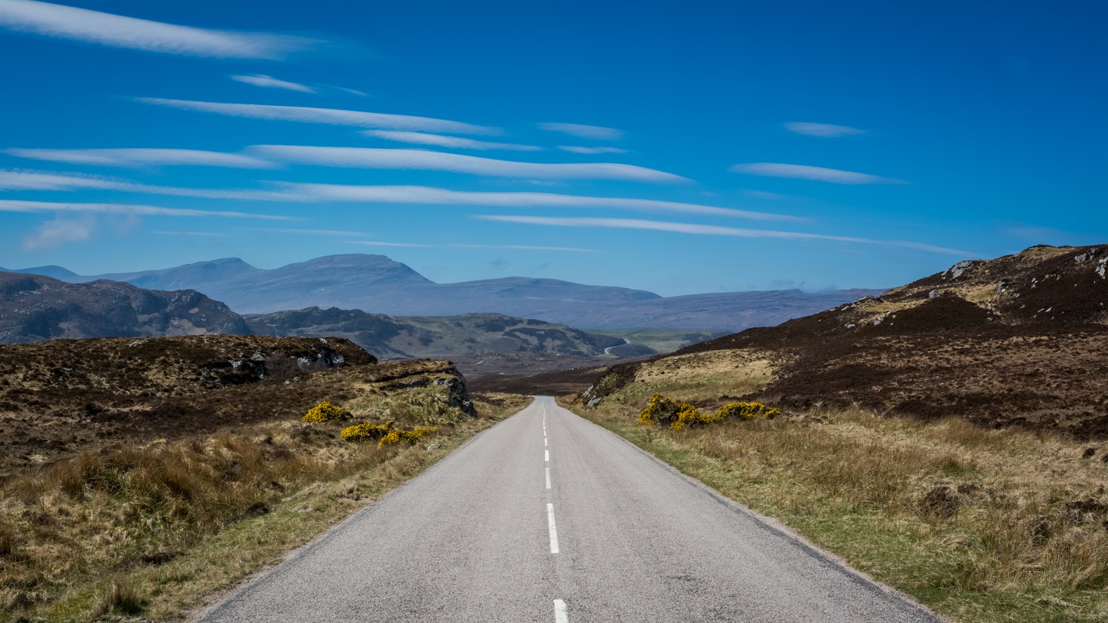The A838 North Coast 500 route descending through Sutherland in the north-west Highlands — we move your bags so you can cycle or hike light